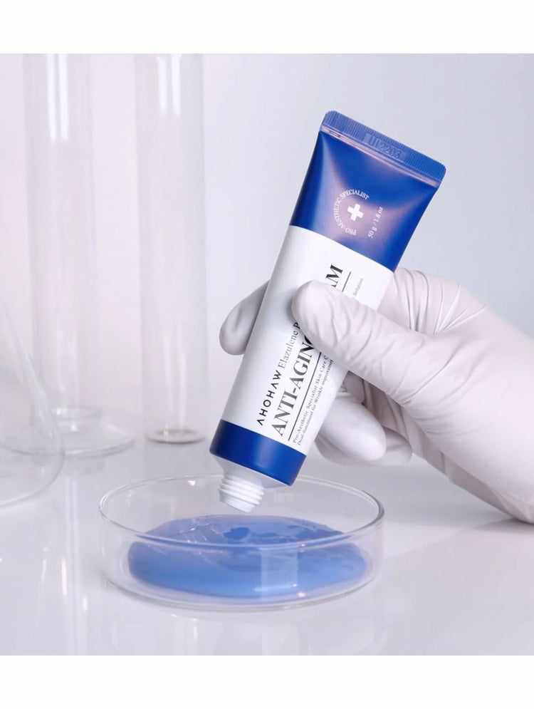 Tube of anti-aging cream held by a gloved hand over a glass dish with blue gel.